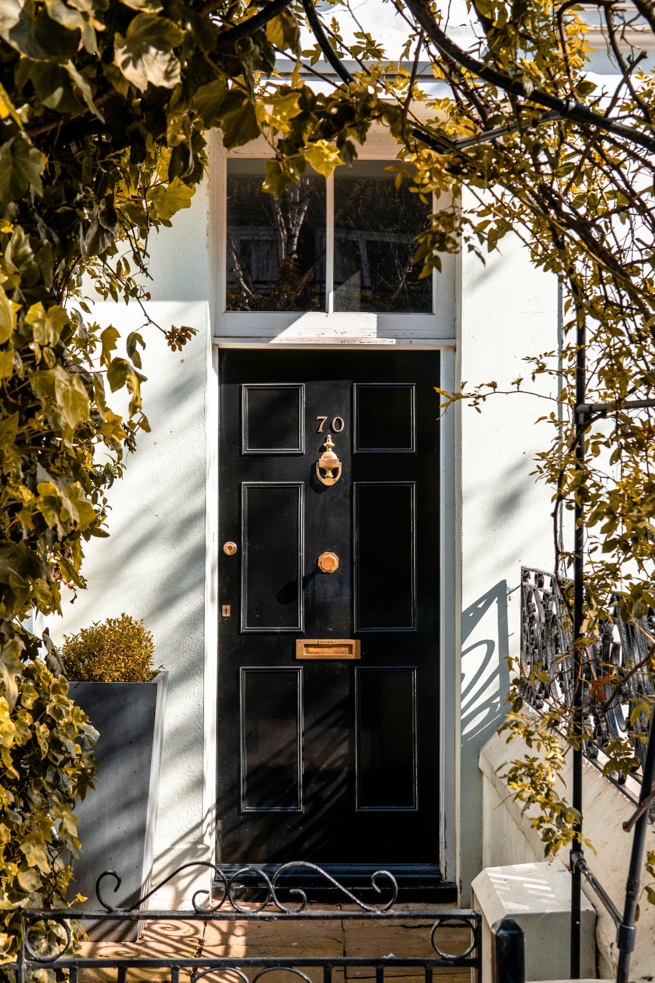 Black front door numbered 70 under an arch of climbing ivy, with a brass knocker and letterbox